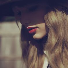 a woman with long blonde hair wearing a fedora and red lipstick on her lips