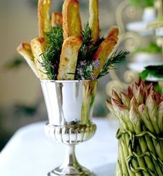 asparagus and other food items are displayed in silver vases on a table