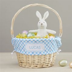 a white bunny sitting in a basket with eggs and an easter egg next to it