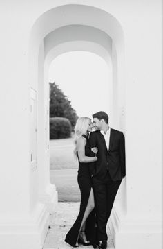 a man and woman standing next to each other in front of a white wall with arches