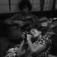 a woman laying on the floor with a guitar and another man sitting next to her