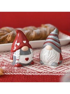 two gnome figurines sitting next to each other on a table with bread in the background