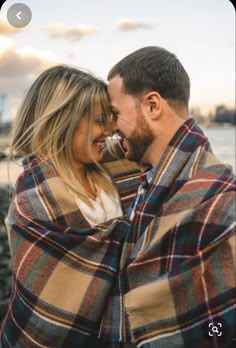 a man and woman wrapped in a blanket by the water with their faces close to each other