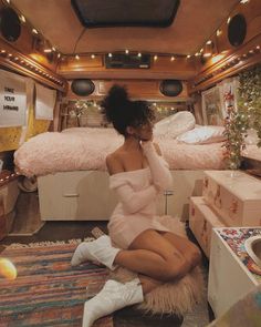 a woman is sitting on the floor in front of a bed and dresser with christmas lights