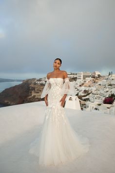 a woman standing on top of a snow covered hillside wearing a white dress with sheer sleeves