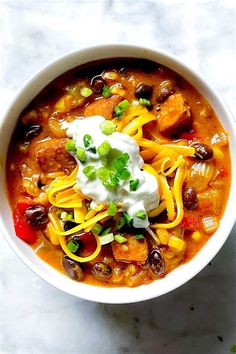 a white bowl filled with chili, beans and sour cream on top of a marble counter