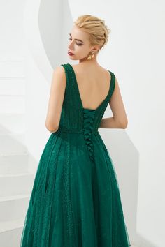 a woman in a green dress standing next to some stairs and looking down at the ground