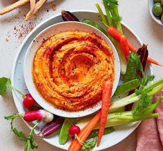 a white plate topped with carrots, celery and hummus next to other vegetables