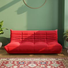 a red futon sofa sitting on top of a wooden floor next to a green wall