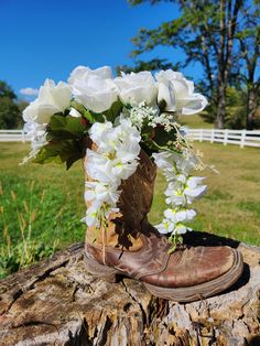 a cowboy boot with flowers in it sitting on a log