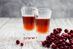 two glasses filled with liquid next to some cranberries