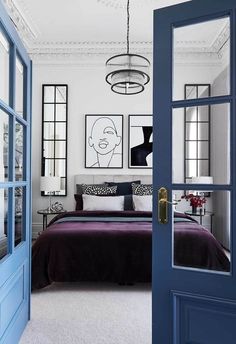 a bedroom with blue doors and pictures on the wall above the bed, along with a purple bedspread