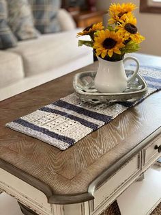 a coffee table with sunflowers in a white vase on it and a blue striped runner