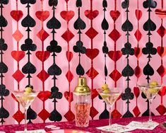 a table topped with two martini glasses filled with liquid next to a wall covered in hearts