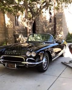 an old black car parked in front of a brick building next to a large tree