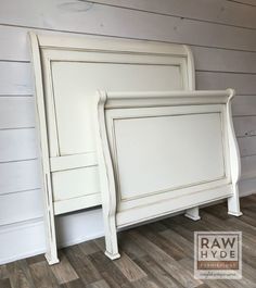 a white bed frame against the wall in a room with wood flooring and walls