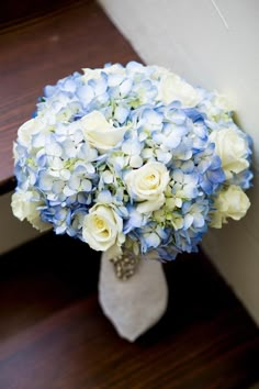 a bouquet of blue and white flowers sitting on top of a wooden floor next to stairs