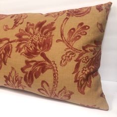 a brown and red floral pillow sitting on top of a white bed