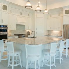 a large kitchen with white cabinets and marble counter tops, along with bar stools