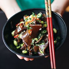 a person holding a bowl of food with chopsticks