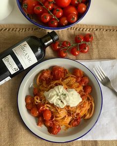 a bowl of spaghetti and tomatoes with a bottle of wine