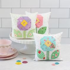 three decorative pillows sitting on top of a white table next to a cup and saucer