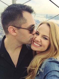 a man and woman kissing each other on the top of a building with a city in the background