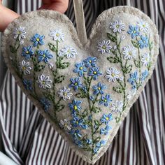 someone holding a heart shaped ornament with daisies and blue flowers on it