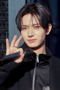 a young man holding a microphone making the peace sign with his hand while wearing a black jacket