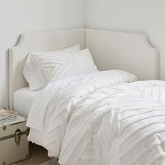 a bed with white comforter and pillows in a room next to a small trunk