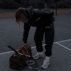 a person bending over with a tennis racket and bag on the ground in front of them