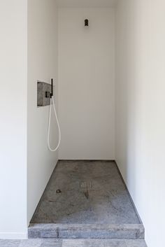 a shower head in the corner of a white room with steps leading up to it