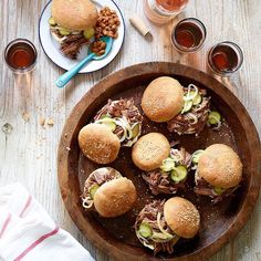 a wooden bowl filled with pulled pork sliders on top of a table next to glasses of tea