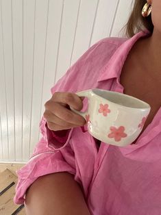 a woman in pink shirt holding a white coffee cup with flower designs on it and gold hoop earrings