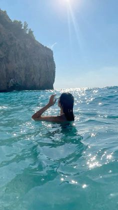 a woman swimming in the ocean next to a cliff