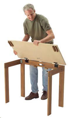 a man standing over a table with a wooden board on it's legs and holding a piece of wood in front of him