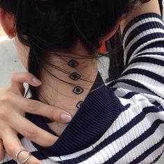 a woman with a neck tattoo on her left side, wearing a striped shirt and silver rings