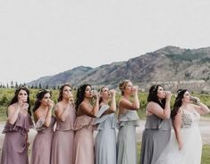 a group of women standing next to each other in front of a mountain range wearing different colored dresses