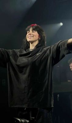 a woman standing on stage with her arms outstretched in the air and smiling at someone behind her