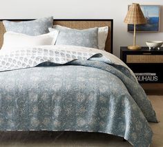 a bed with blue and white bedspread next to a lamp on a nightstand