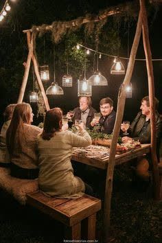 a group of people sitting around a wooden table eating food and drinking wine at night