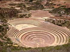 an aerial view of a circular stone structure in the middle of a field with trees and mountains in the background