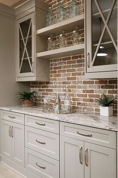 a kitchen with white cabinets and marble counter tops in front of a brick backsplash