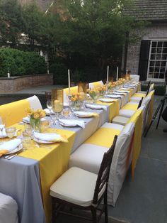 a long table is set with yellow and white linens for an outdoor dinner party