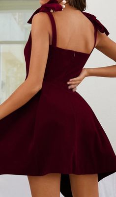 a woman in a short maroon dress is posing with her back to the camera and hands on her hips