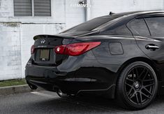 the rear end of a black car parked in front of a white building with graffiti on it