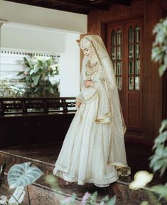 a woman in a white wedding dress and veil is standing on the steps near a bench