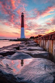 a light house sitting on top of a rocky shore next to the ocean at sunset