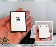 a hand holding a small white box with a chanel logo on the front and back side