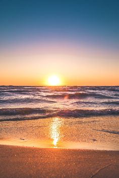 the sun is setting over the ocean with waves coming in to shore and sand on the beach